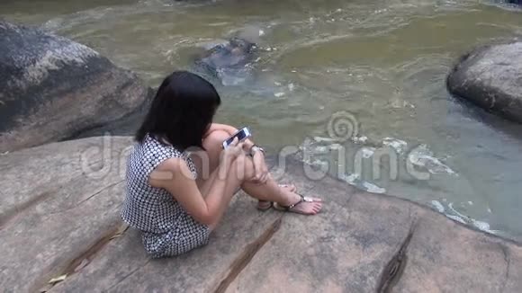 使用智能手机户外活动的女人坐在瀑布旁微笑视频的预览图
