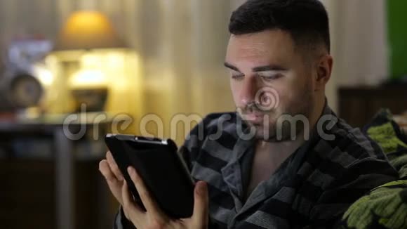 一平板电脑的男人坐在家里的沙发上视频的预览图