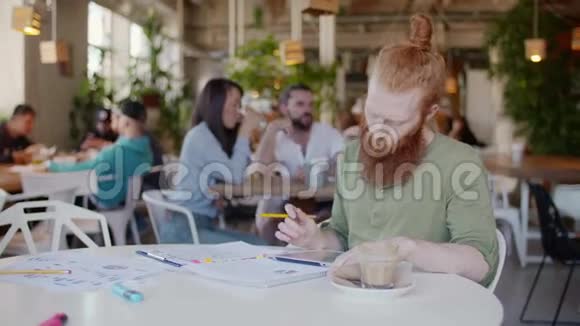 姜男在咖啡馆工作在桌子上的图表和帕珀在他身后有一群快乐的年轻人视频的预览图