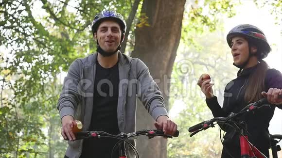 漂亮的夫妇在秋天的公园里骑自行车散步慢动作视频的预览图