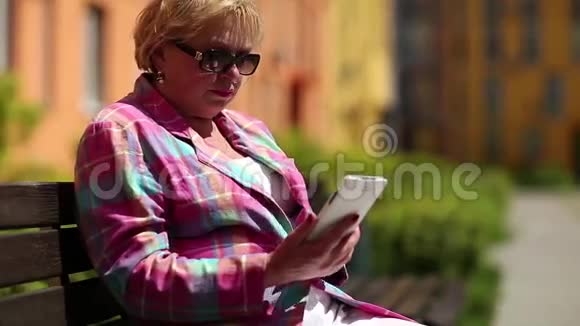 女人坐在院子里的长凳上用白色智能手机视频的预览图