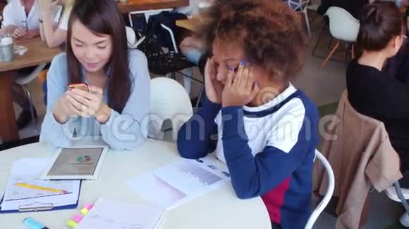 两个快乐的女孩亚裔和黑人在咖啡馆里聊天和工作视频的预览图