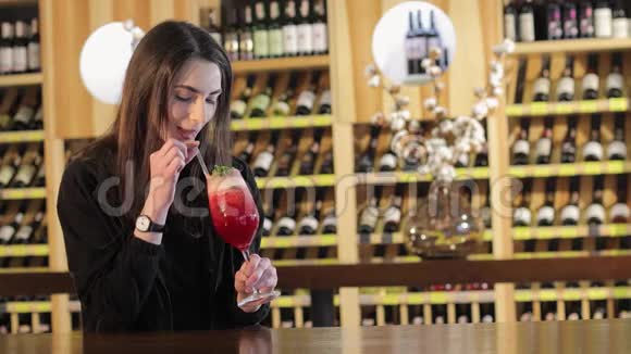 一个女孩在酒吧喝一杯红色鸡尾酒女人喝红色异国情调的鸡尾酒视频的预览图