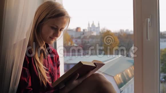一位快乐的年轻女子她家坐在窗台上视频的预览图