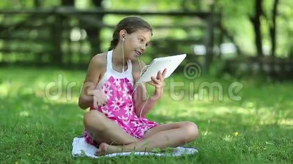 漂亮的女孩带着平板电脑坐在花园的草地上视频的预览图