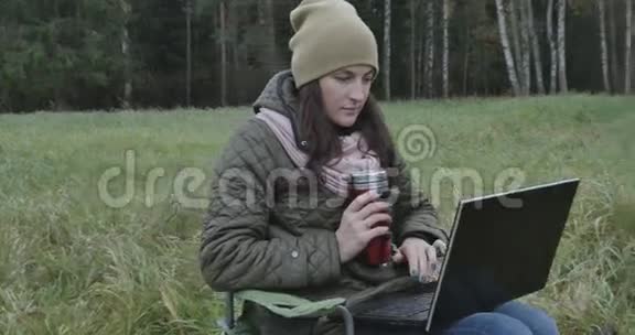 年轻的深色头发的女学生在大自然中做笔记本电脑美丽的秋日和女人在使用笔记本电脑时享受它视频的预览图