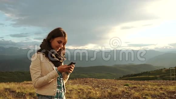 女人徒步旅行者在日落山峰崖用手机视频的预览图
