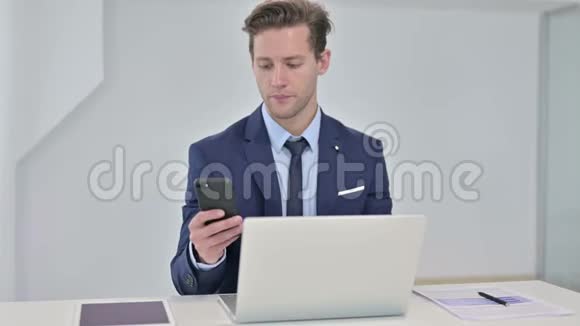 严肃的年轻商人在手提电脑和智能手机上聊天视频的预览图