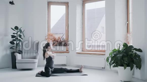 穿着运动服的年轻黑发女孩在家里的明亮房间里做运动视频的预览图
