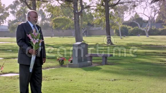 非裔美国人中老年男性在墓地中与鲜花站在一起视频的预览图