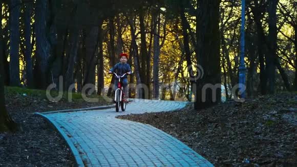 小男孩在公园里骑自行车日落公园慢动作视频的预览图