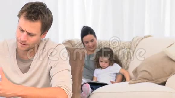 一个愤怒的男人看着他的家庭账单而他的家人在沙发上视频的预览图