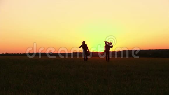 两个农民拿着铲子走在田野上他们携带种植树木的设备在日落的时候侧视图视频的预览图