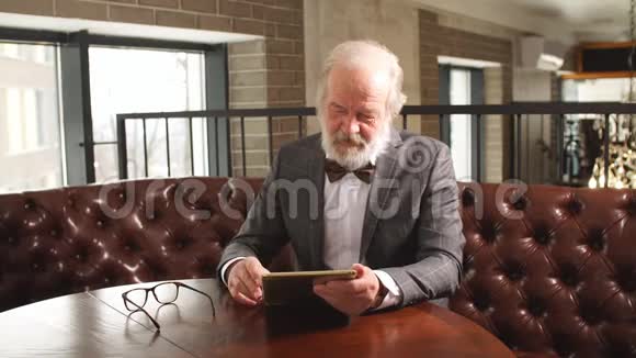 英俊的老人在家庭办公室做数字平板电脑视频的预览图