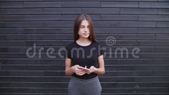 一位漂亮的年轻女士戴着眼镜用手机对着砖墙背景特写镜头视频的预览图