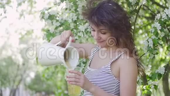 一个女人在苹果的背景下从罐子里倒果汁视频的预览图