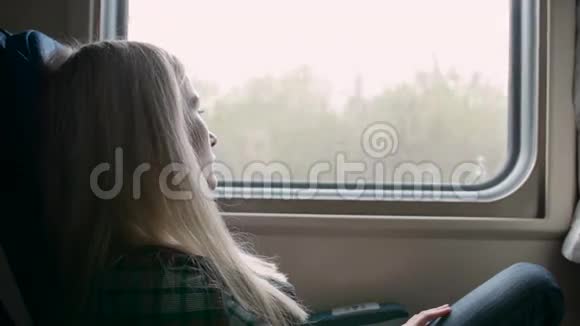 年轻的白种人女人坐火车旅行时透过窗户看视频的预览图