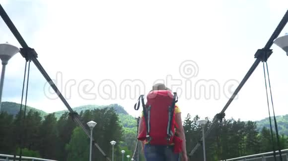 那个带着红色背包的旅行者的女人沿着斜拉桥穿过山河视频的预览图