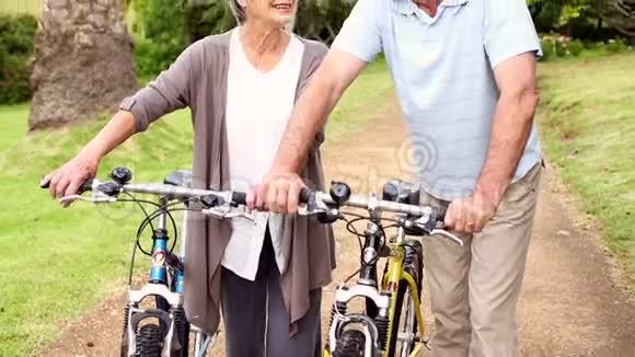 一对退休夫妇骑着自行车站在公园里视频的预览图