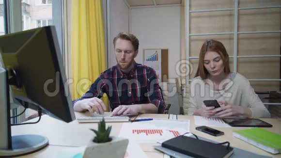 男人专心工作在电脑前女人看着智能手机视频的预览图