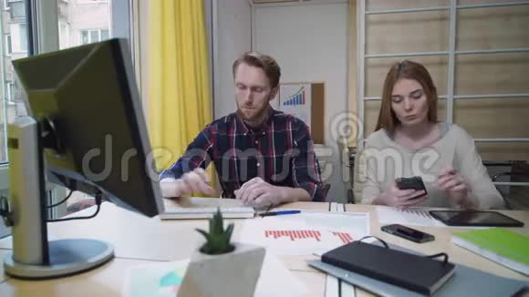 男人专心工作在电脑前女人看着智能手机视频的预览图