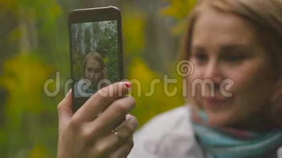 一位有魅力的女士在晚上穿过公园时用手机拍照视频的预览图