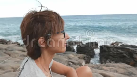 有眼镜和红毛的成年女性肖像在背景中摇摆的海洋离焦视频的预览图