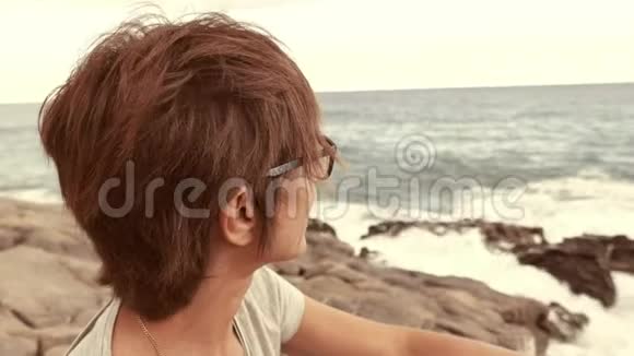 有眼镜和红毛的成年女性肖像在背景中摇摆的海洋离焦视频的预览图
