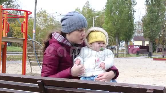 年轻的母亲带着孩子坐在公园的长凳上视频的预览图