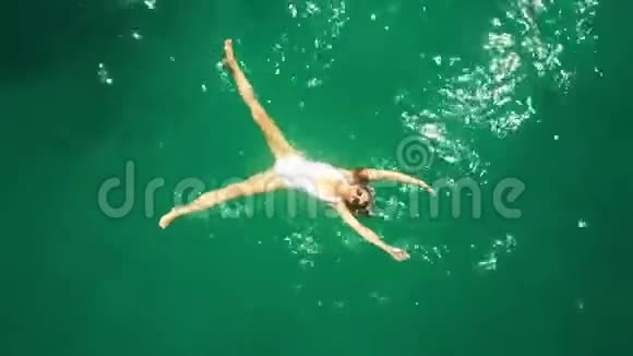 一位身穿白色泳衣在海中沐浴的年轻美女的高空俯视图视频的预览图