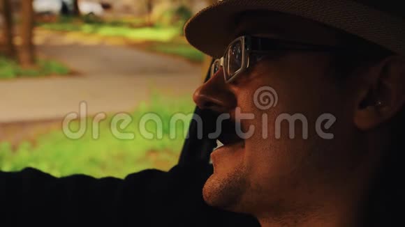 戴着胡子戴着帽子的人戴着眼镜坐在车里唱歌仿写希普斯特视频的预览图