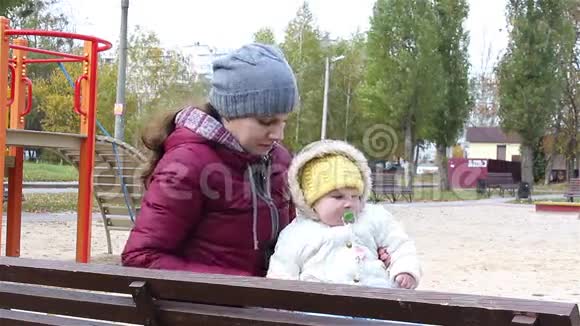 年轻的母亲带着孩子坐在公园的长凳上视频的预览图