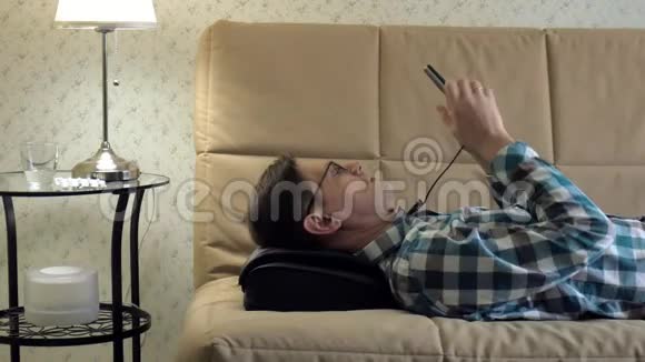 男人躺在家里的沙发上躺在按摩器的头下放松的状态视频的预览图