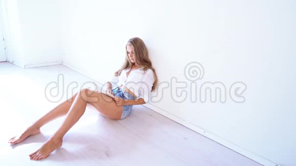 一个漂亮的女孩坐在白色的房间里看书视频的预览图