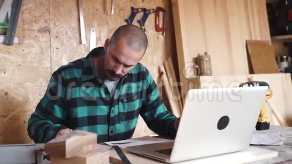 一位留着老式胡子的大胆木匠在车间工作时使用了一台笔记本电脑视频的预览图