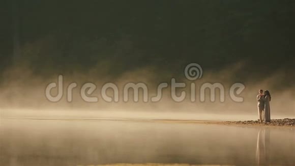 一对身穿乌克兰民族服装的乡村夫妇在夕阳的金色薄雾中温柔地拥抱在岩石海岸上视频的预览图