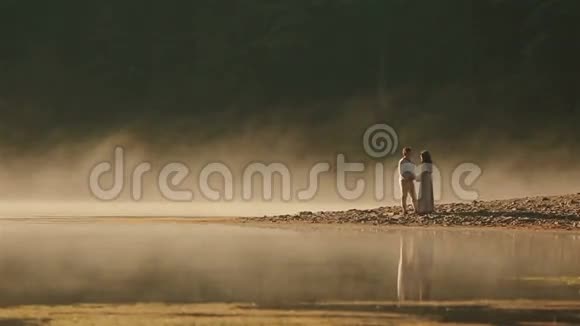 一对身穿乌克兰民族服装的乡村夫妇在夕阳的金色薄雾中温柔地拥抱在岩石海岸上视频的预览图