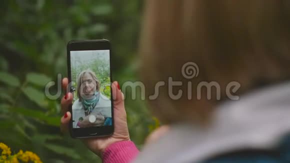 一位有魅力的女士在晚上穿过公园时用手机拍照视频的预览图