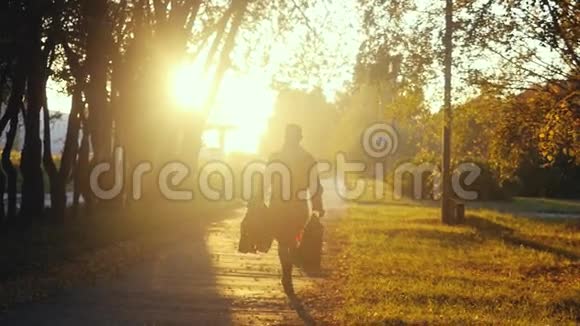 年轻女子穿着雨衣带着购物袋在日落时慢慢地在公园里晒太阳1920x1080视频的预览图