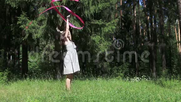穿灰色衣服的年轻女子在夏天的森林里用丝带跳舞视频的预览图