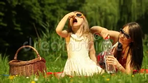 野餐女孩子喝水妈妈在草地上用平板电脑视频的预览图