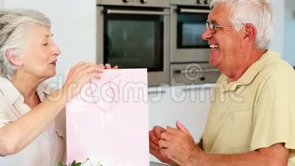 一位老人给他的搭档一个粉红色袋子里的礼物视频的预览图