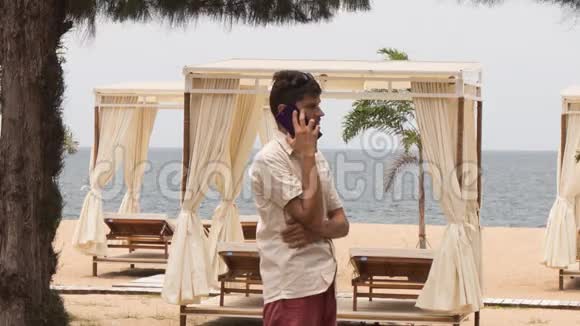 盖伊在海滩上对着帐篷下的日光浴床打电话视频的预览图
