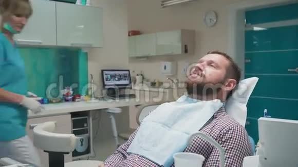 女性牙医检查男性患者的牙齿并寻找相机视频的预览图