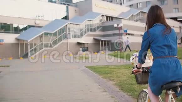 在城市里一个头发长长的黑发女孩骑着一辆自行车花篮里放着花慢慢地稳健地拍着视频的预览图