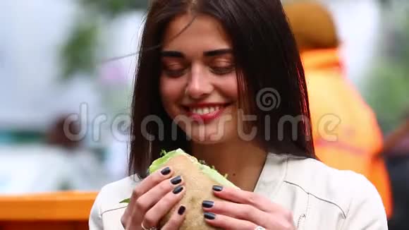 年轻女子在户外咖啡馆吃三明治在咖啡馆吃三明治的漂亮女人有魅力的女人在公园吃三明治视频的预览图