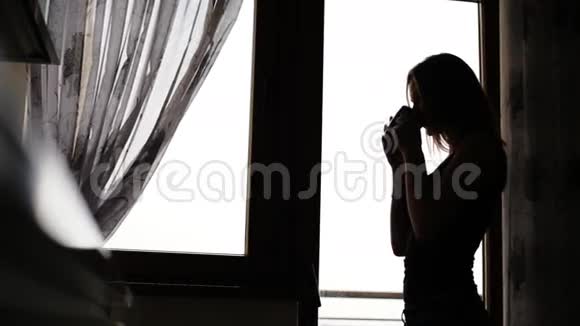 迷人的年轻女士休息在家的窗户前喝一杯茶或咖啡视频的预览图