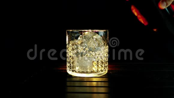 酒吧老板把威士忌倒在杯子里木桌上放冰块黑黑的背景重点放在冰块上威士忌放松时间视频的预览图