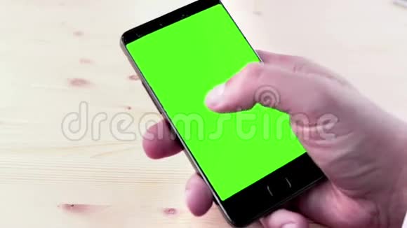 男人用智能手机写短信用色度键绿色屏幕在木桌上视频的预览图