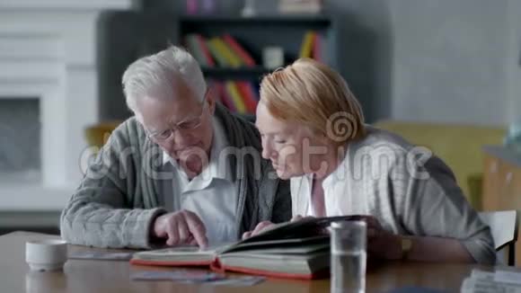 年长的幸福夫妇在一起怀旧他们看着旧相册微笑着视频的预览图